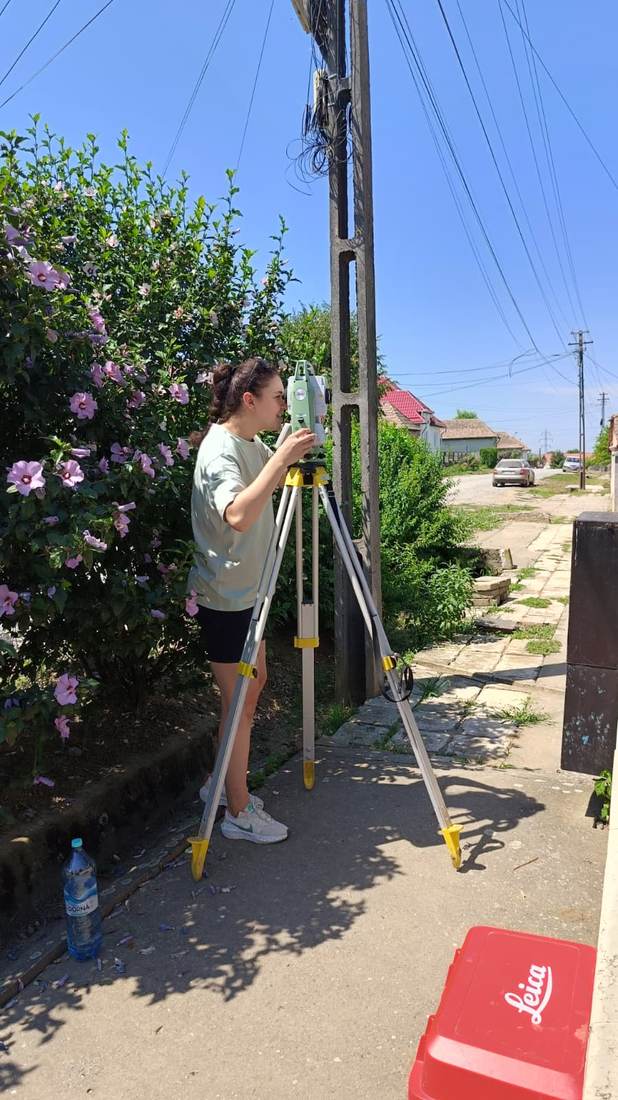 Membru al echipei realizând măsurători cu stație totală, pe o alee dintr-o localitate.