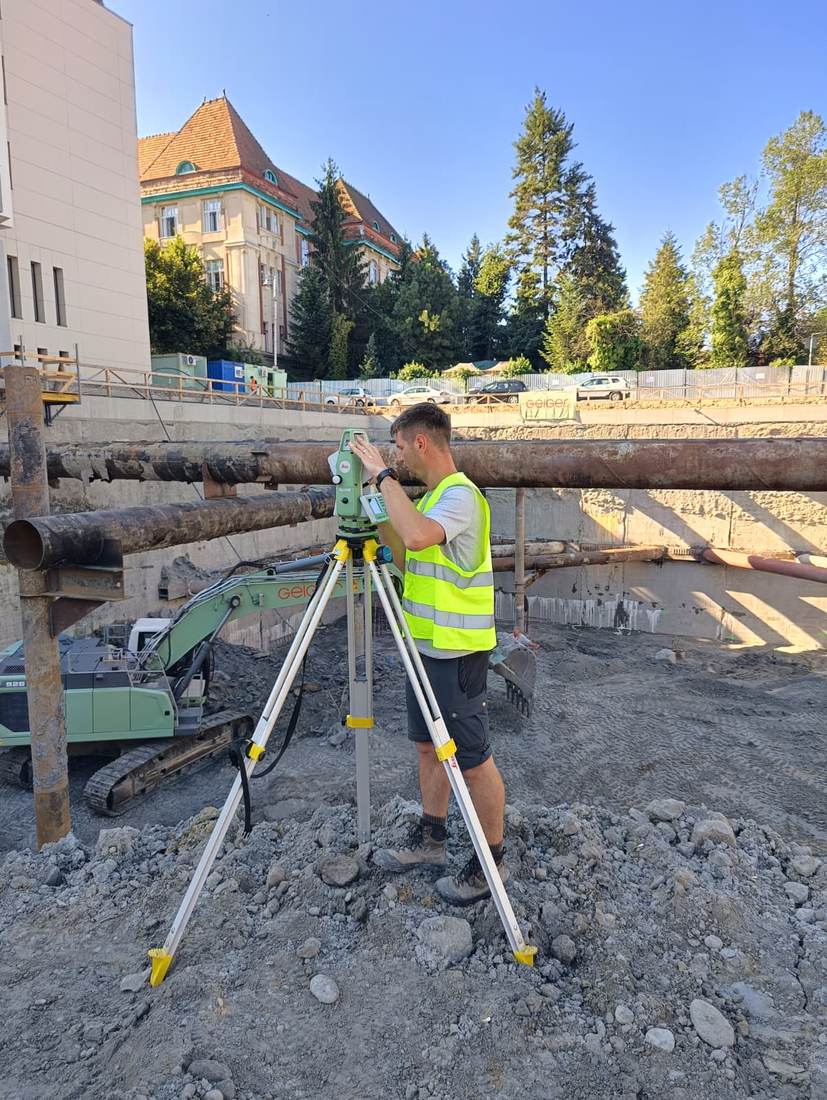 Inginer topograf efectuând măsurători cu stație totală pe un șantier de excavare, în centrul orașului.
