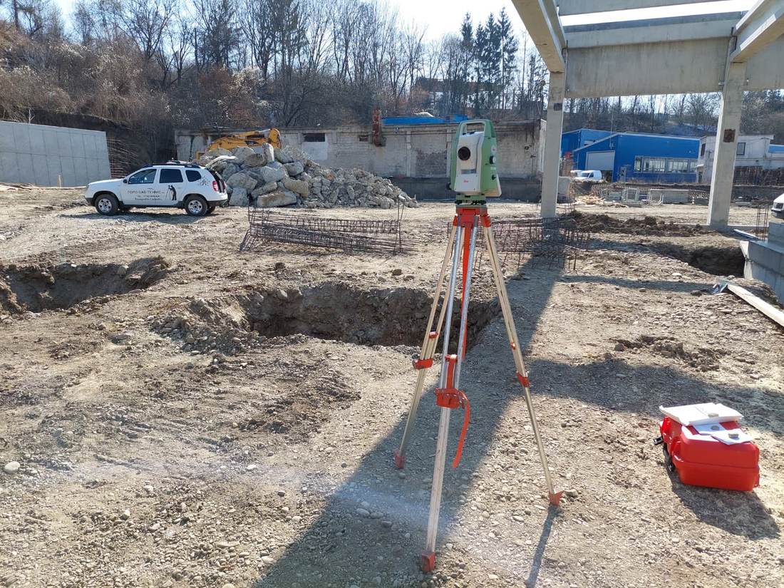 Stație totală amplasată sub o structură în construcție, cu autoturismul echipei parcat în fundal.