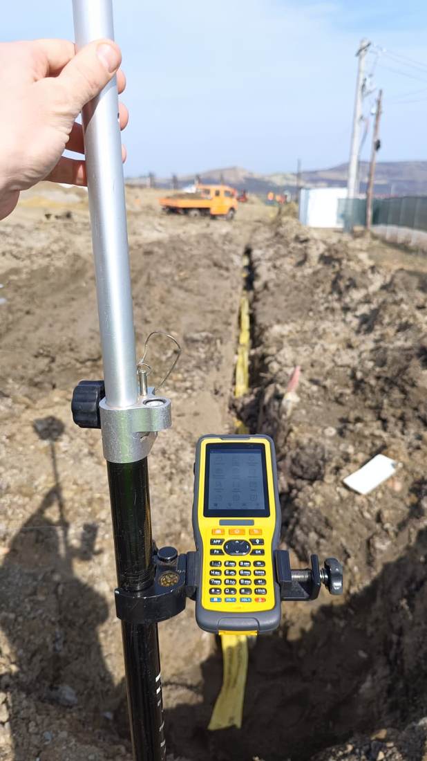 Colector de date GPS montat pe jalon, folosit pentru trasarea unei conducte într-un șanț de excavare.